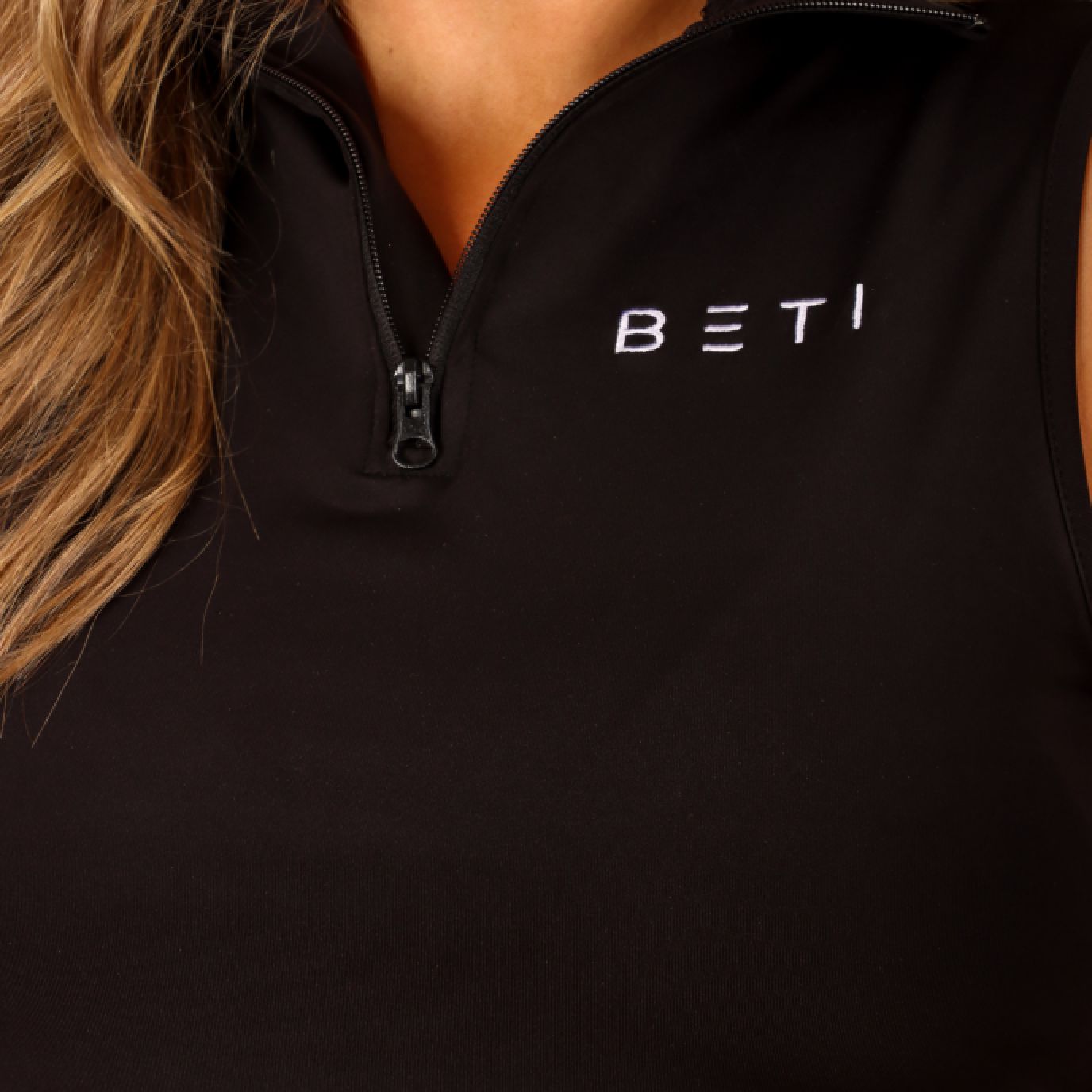 A close up shot of the always black zip up vest and the precise embroidering of the BETI logo